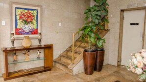 Un escalier avec une rampe en verre, une plante en pot et un vase posé sur une console.