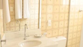 Un baño con lavamanos, espejo y retrete blancos. Hay dos toallas colgadas en la pared.