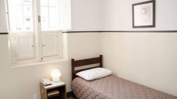 Quarto pequeno com uma cama de solteiro, cabeceira de madeira, luminária de cabeceira e um quadro na parede.