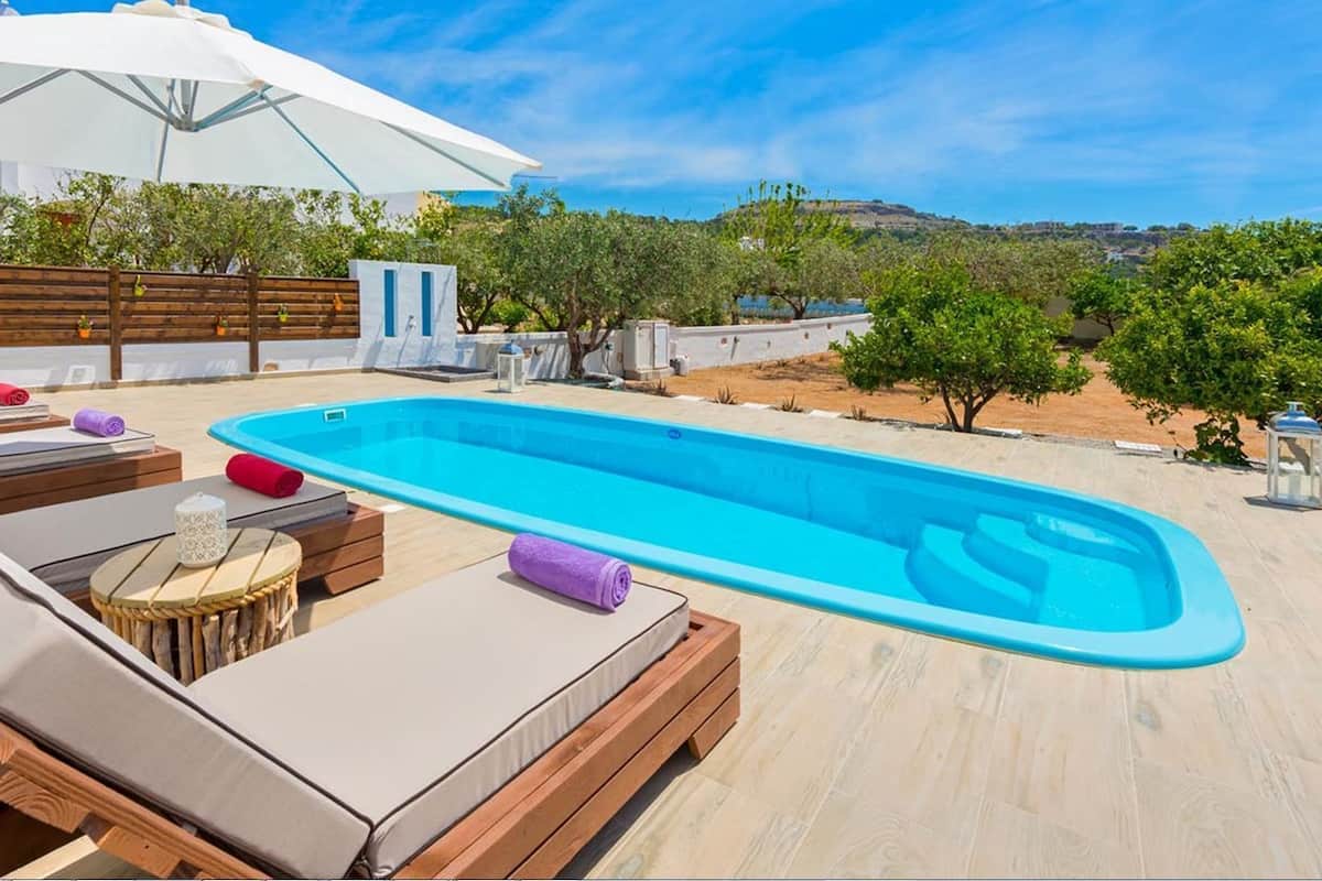 A swimming pool with lounge chairs and umbrellas, surrounded by a wooden deck and greenery.