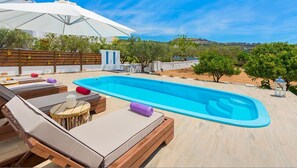 A swimming pool with lounge chairs and umbrellas, surrounded by a wooden deck and greenery. - Melfe Villas (Rhodes)