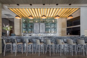 Una zona de bar con encimera de mármol, varios taburetes altos e iluminación colgante.