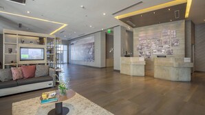Een moderne lobby met een receptiebalie, een bank met kussens, een salontafel en een televisiescherm.
