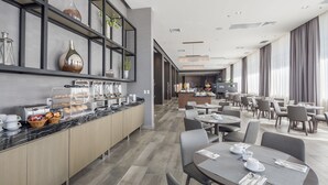 Een moderne hotellobby met een centrale bar, zitgedeeltes en een ontbijtbuffet.
