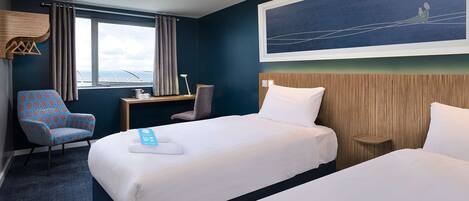 A hotel room with two beds, a desk, a chair, and a large window.