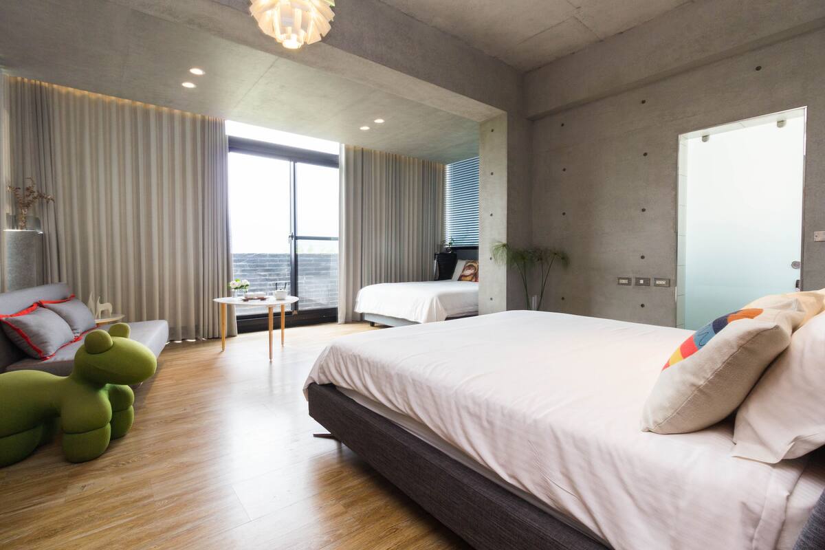 A modern hotel room with a large bed, a sofa, a small table, and a view of the city.