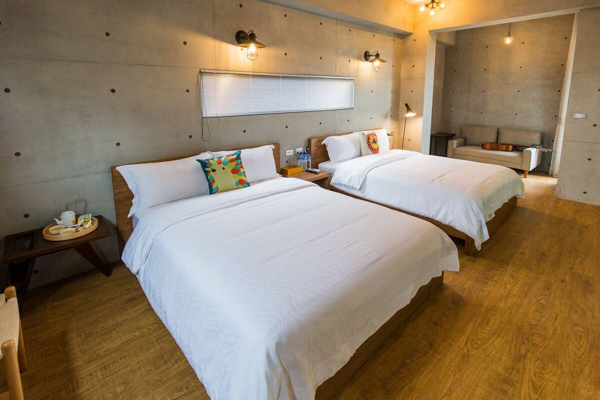 A hotel room with two beds, a wooden floor, a sofa, and a small table with a tray of breakfast.