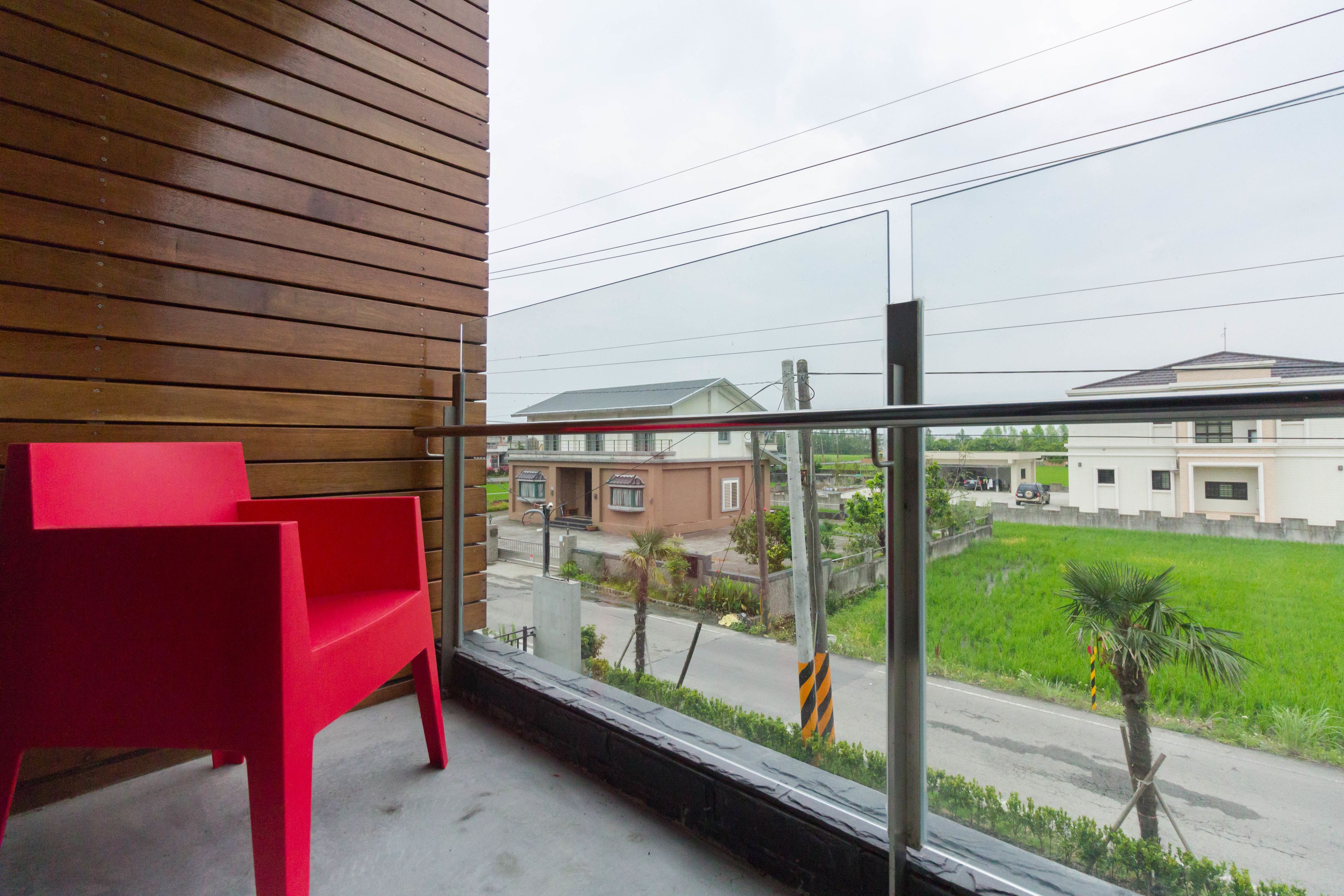 A balcony with a red chair, a view of a road, and buildings in the background.