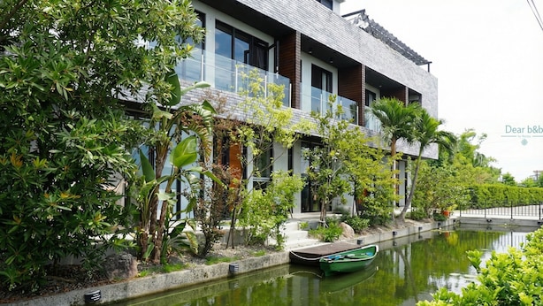 A modern building with a glass balcony, a small dock with a boat, and a water canal. - Sunrise Bed and Breakfast (Dongshan)