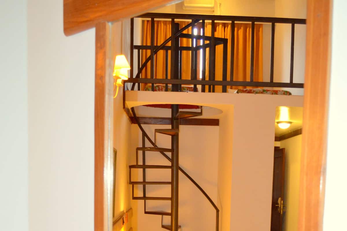 Ein Schlafzimmer mit Holz-Kopfteil, einem Bett mit Blumenmuster-Bettwäsche, einer Treppe und einem kleinen Fenster mit Vorhängen.