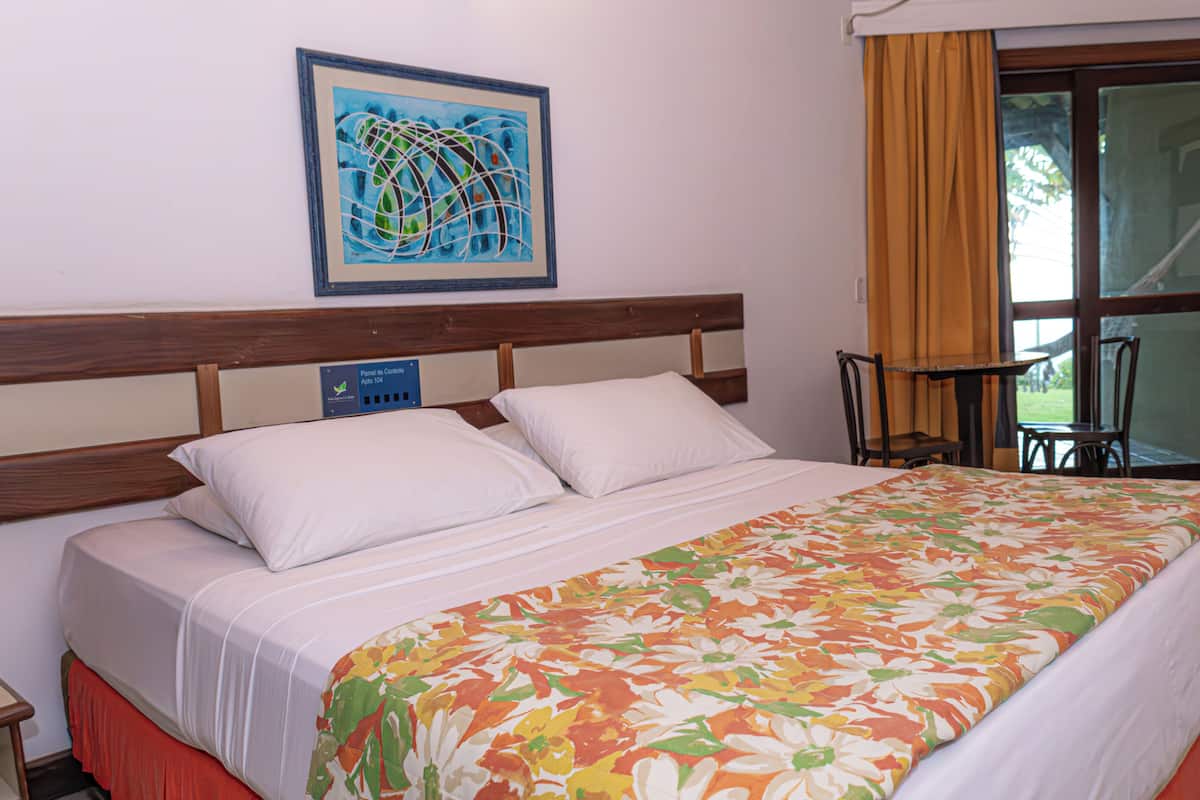 Ein Hotelzimmer mit Bett, Bedienfeld, Fenster mit Vorhängen und einem kleinen Tisch.
