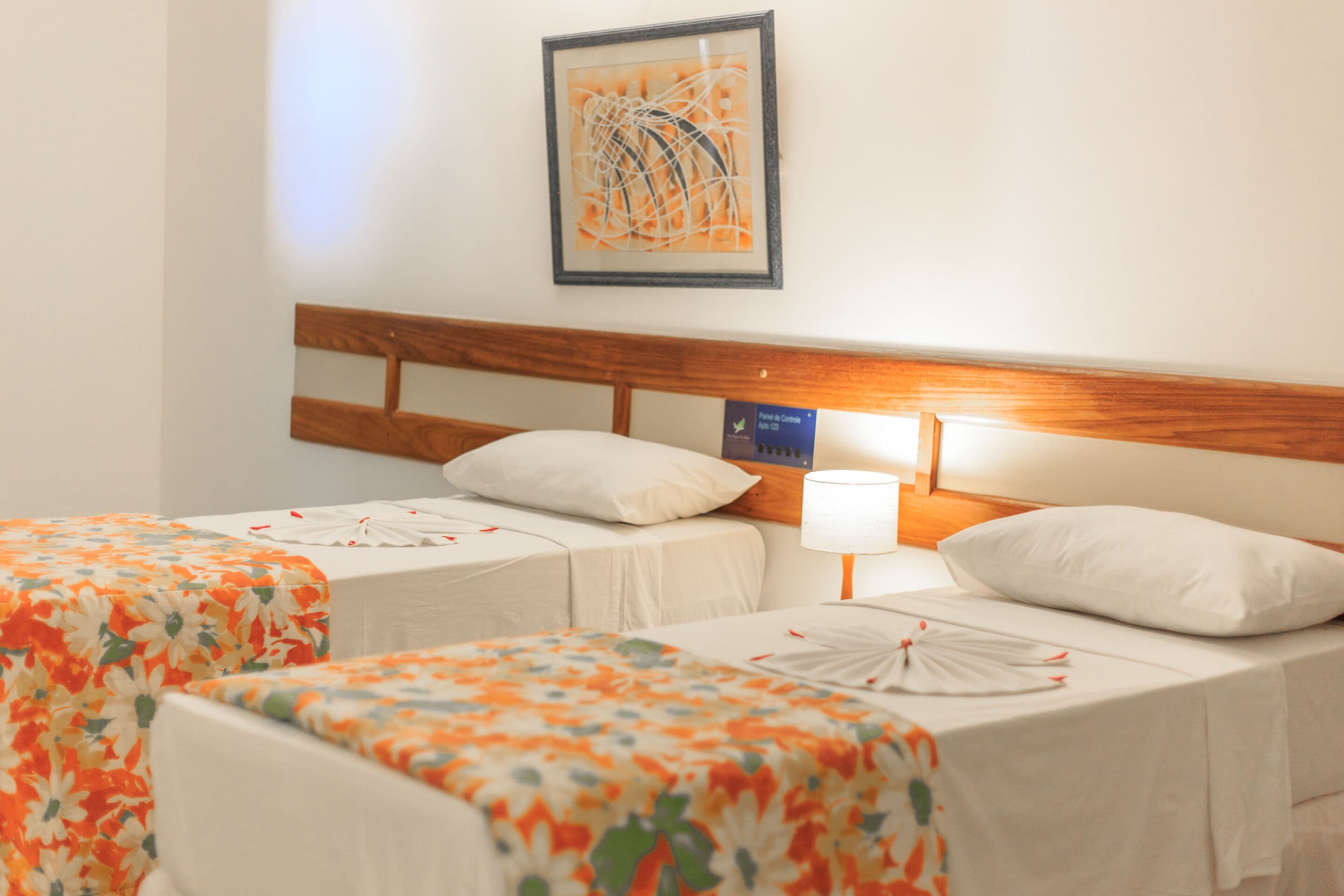 Een hotelkamer met twee bedden, elk met een bloemenprint beddeken, een houten hoofdeinde en een lijst met een abstract schilderij aan de muur.