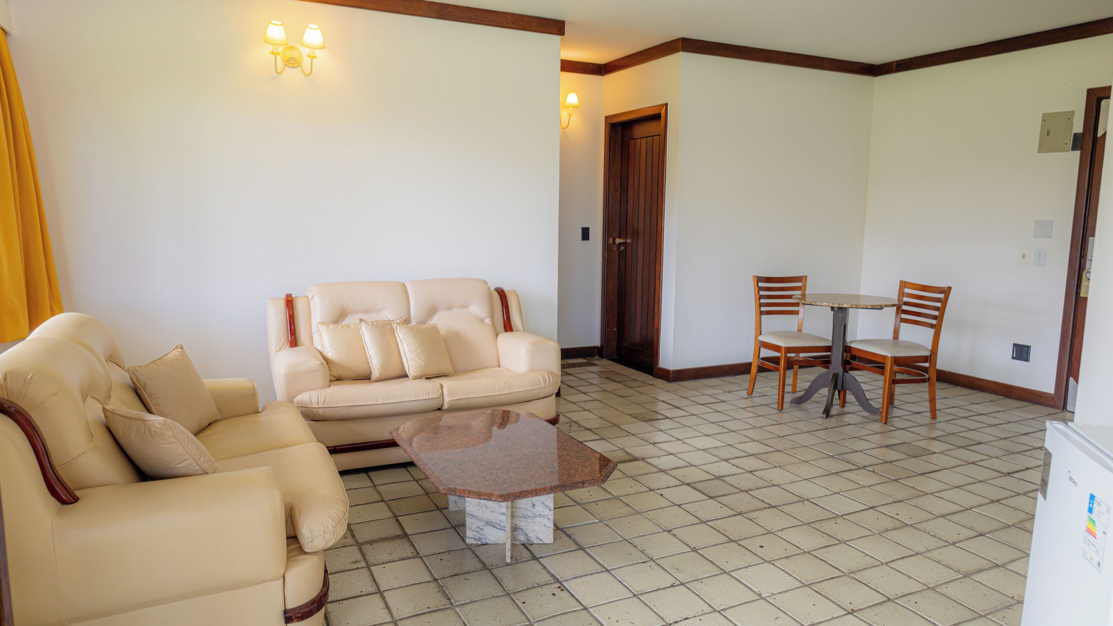 A living room with a beige sofa, a coffee table, and a dining area with two wooden chairs and a small table.