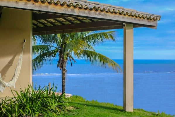 Una estructura frente a la playa con una hamaca, una palmera y vista al océano.