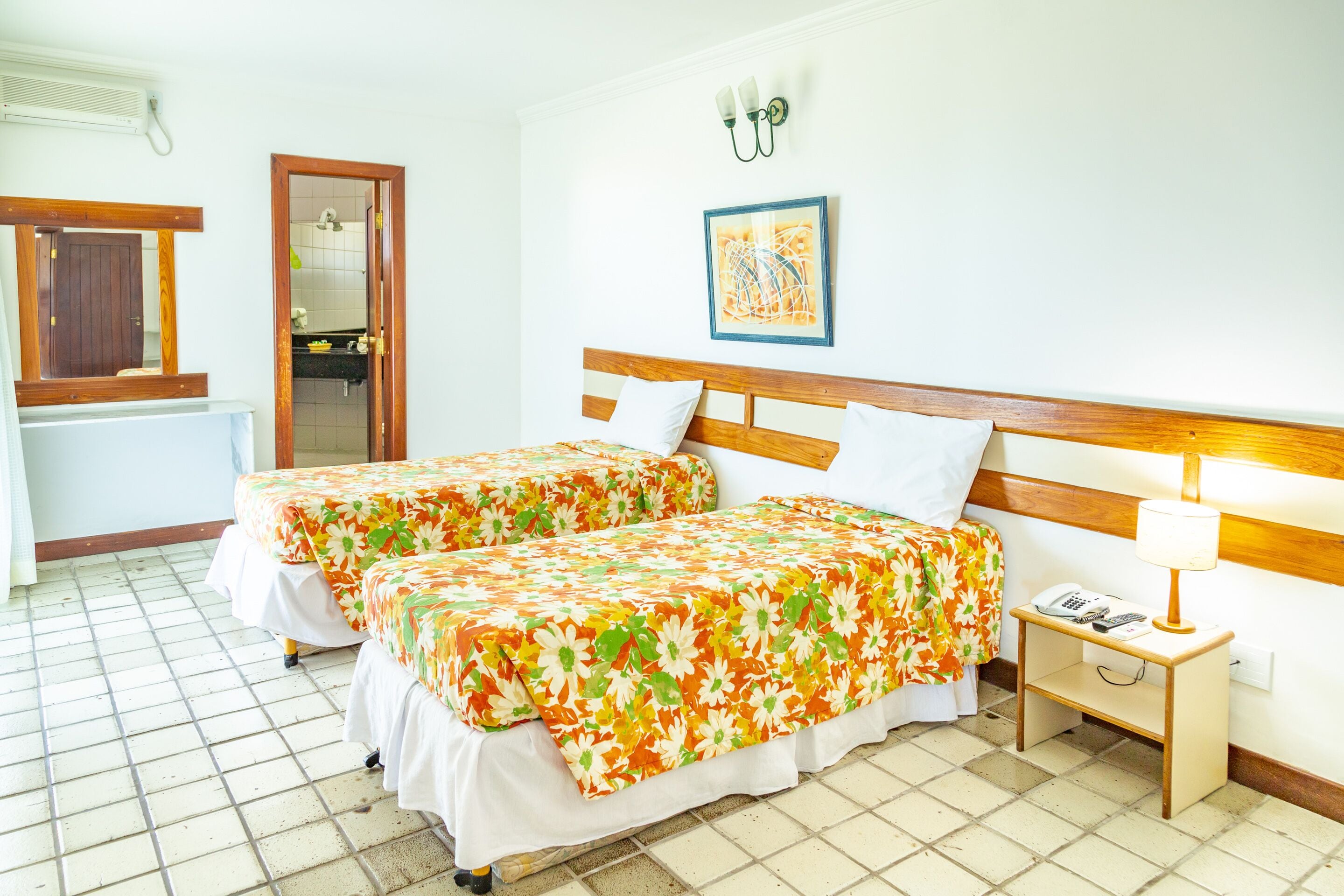 A hotel room with two beds, a nightstand, a mirror, a picture on the wall, and a tiled floor.
