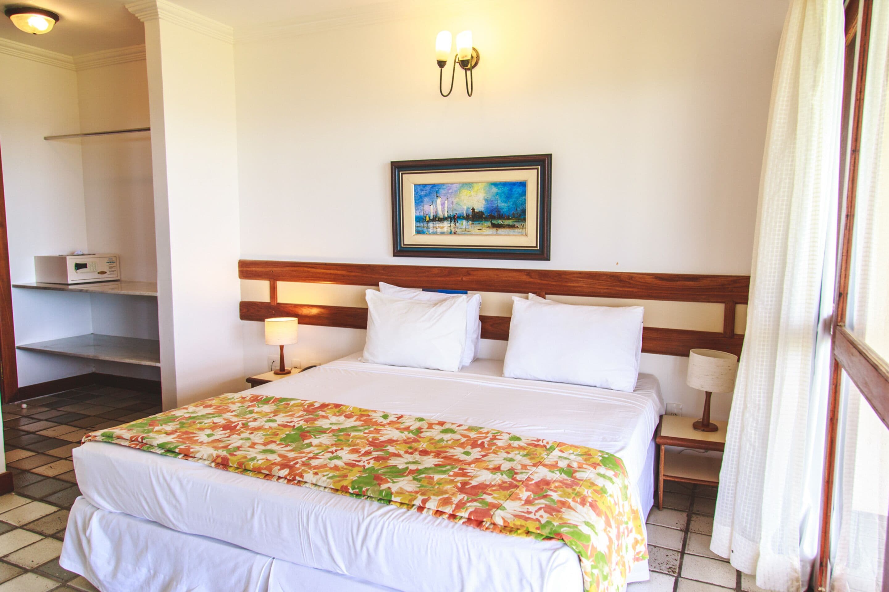 A hotel room with a large bed, a painting on the wall, a nightstand, and a lamp.