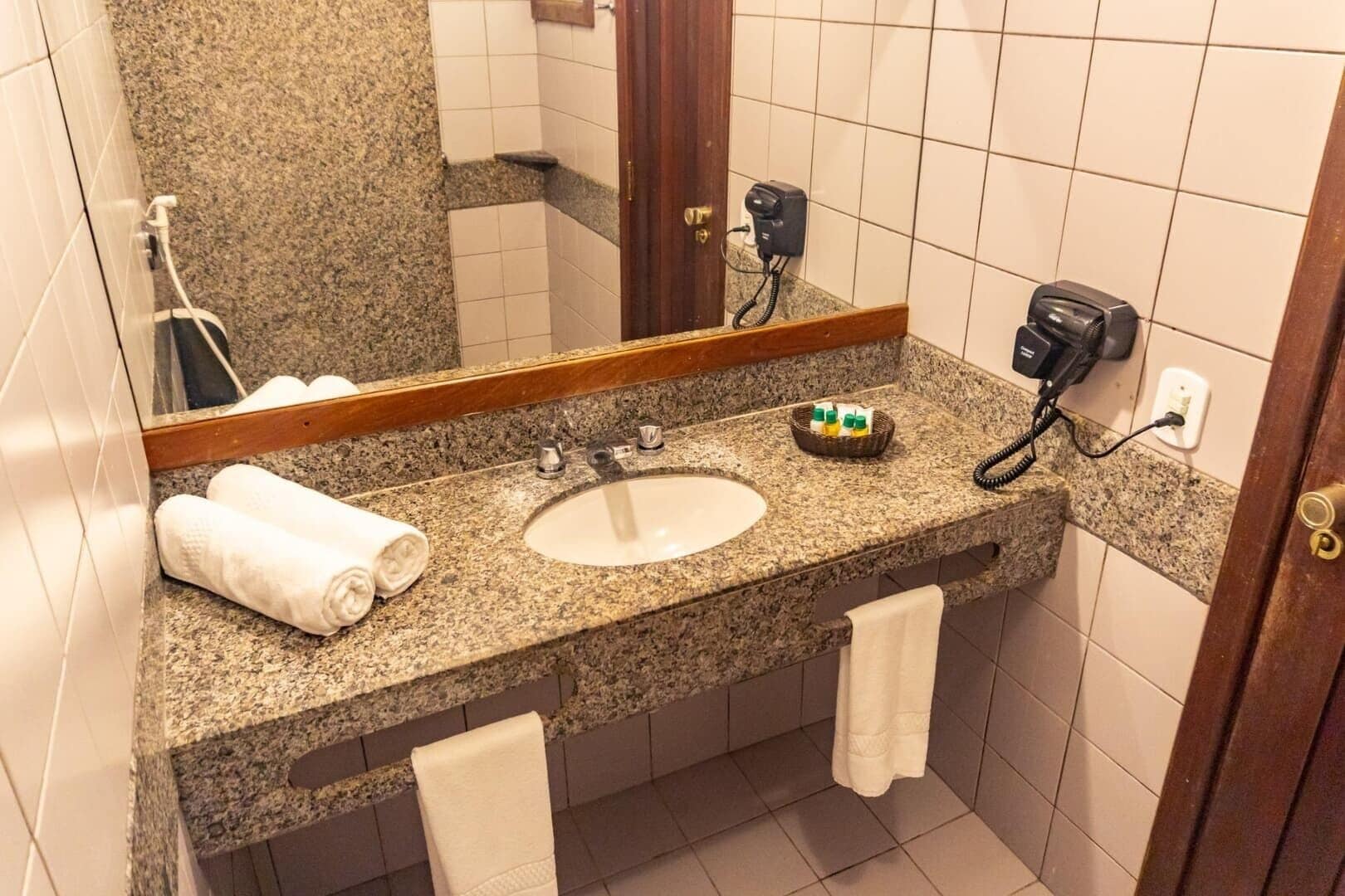 Un baño con encimera de granito, un lavamanos blanco, un espejo y un secador de pelo en la pared.