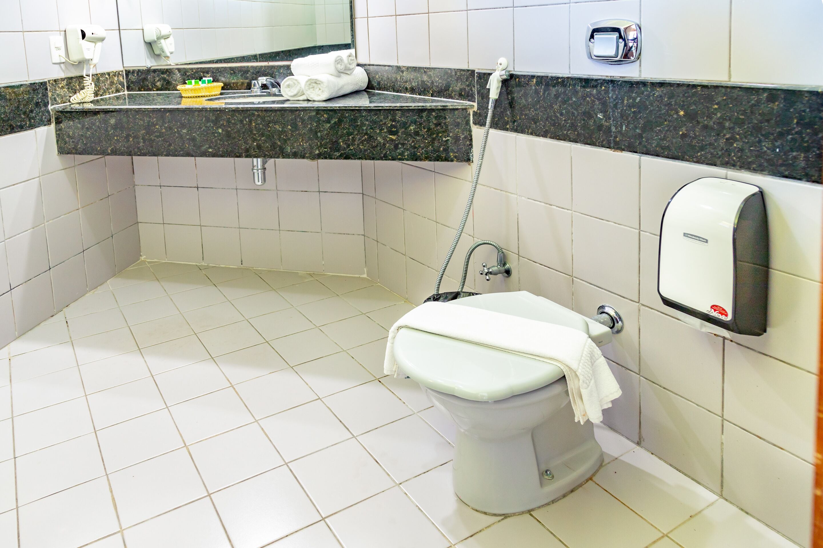 A bathroom with a toilet, a sink with a towel rack, and a soap dispenser.