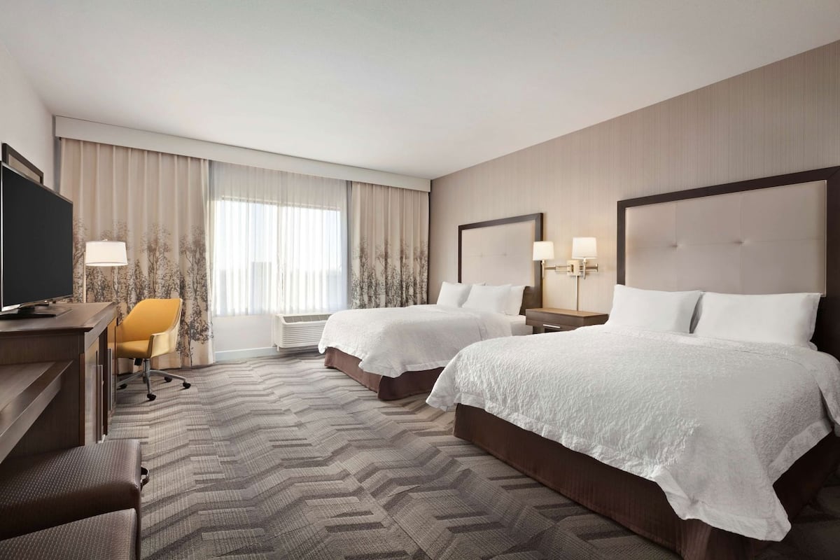 A hotel room with two beds, a desk, a chair, a television, and a window with curtains.