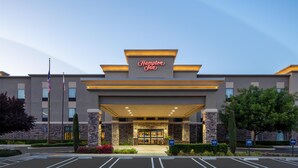 A Hampton Inn hotel entrance with a modern facade, stone pillars, and a clear sky.