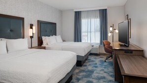 A hotel room with two beds, a desk with a TV, a chair, and a large window with curtains.