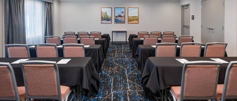 Un salón de conferencias con mesas y sillas, piso alfombrado y dos cuadros en la pared.