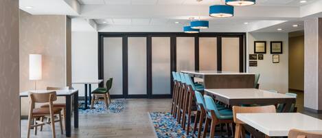 Un comedor moderno con varias mesas y sillas, un tapete estampado y lámparas colgantes azules.