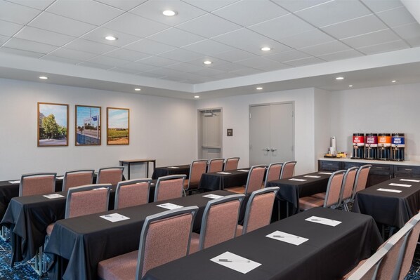 A conference room with tables, chairs, and a buffet area with labeled food options.
