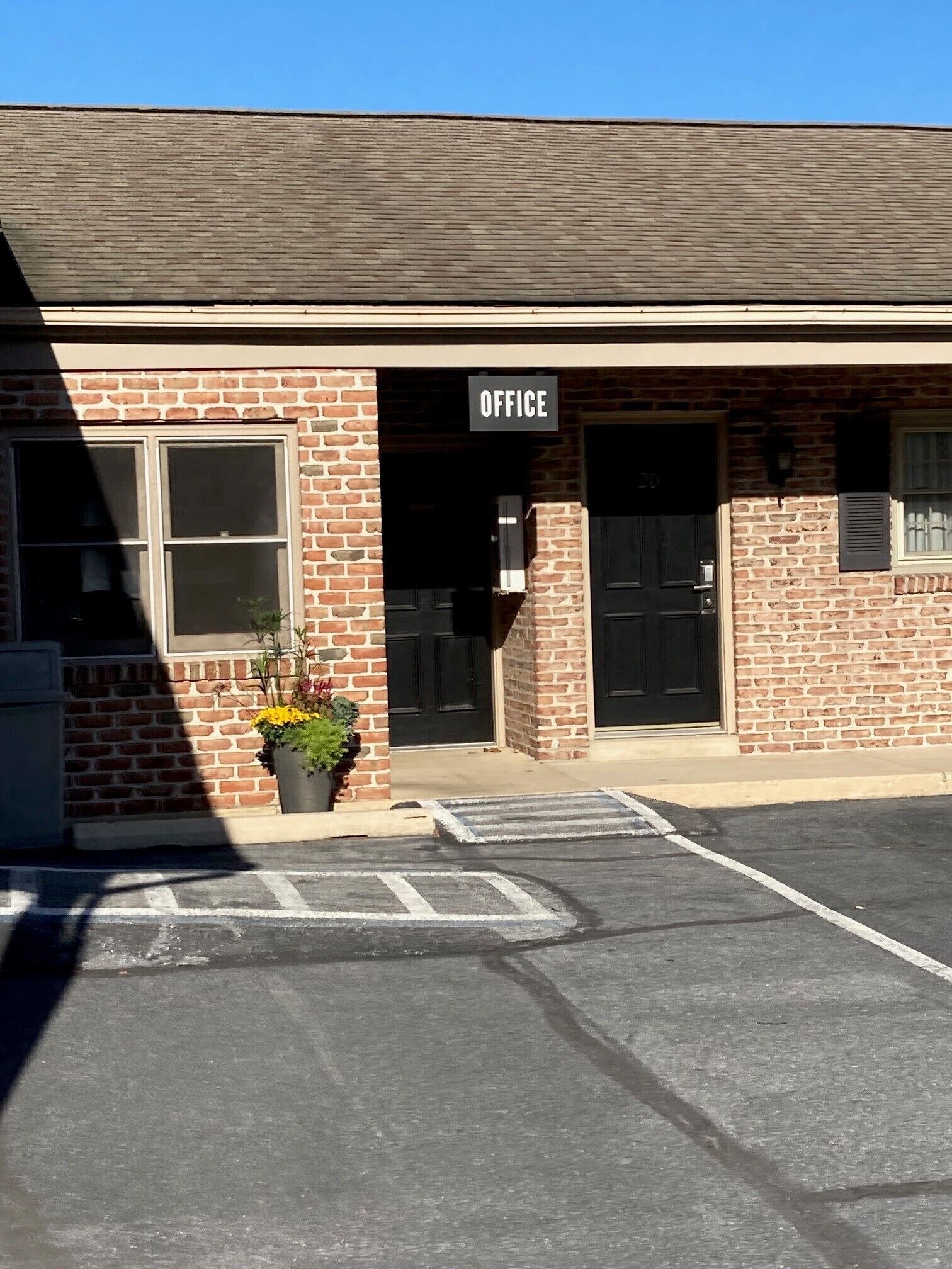 A brick building with a sign reading "OFFICE" above the entrance. There is a potted plant in front of the building.