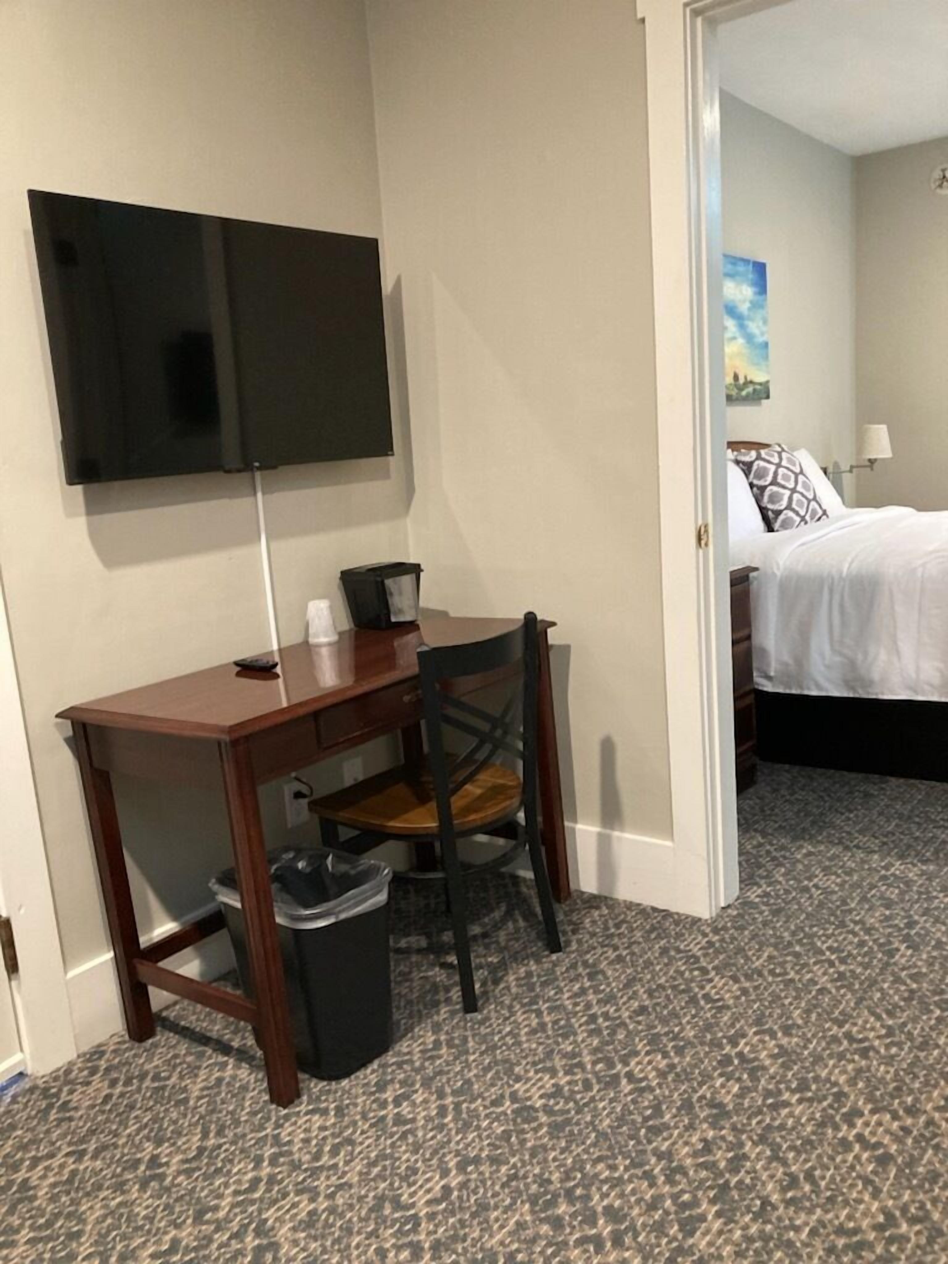 Ein Hotelzimmer mit Schreibtisch, Stuhl und einem an der Wand befestigten Fernseher.