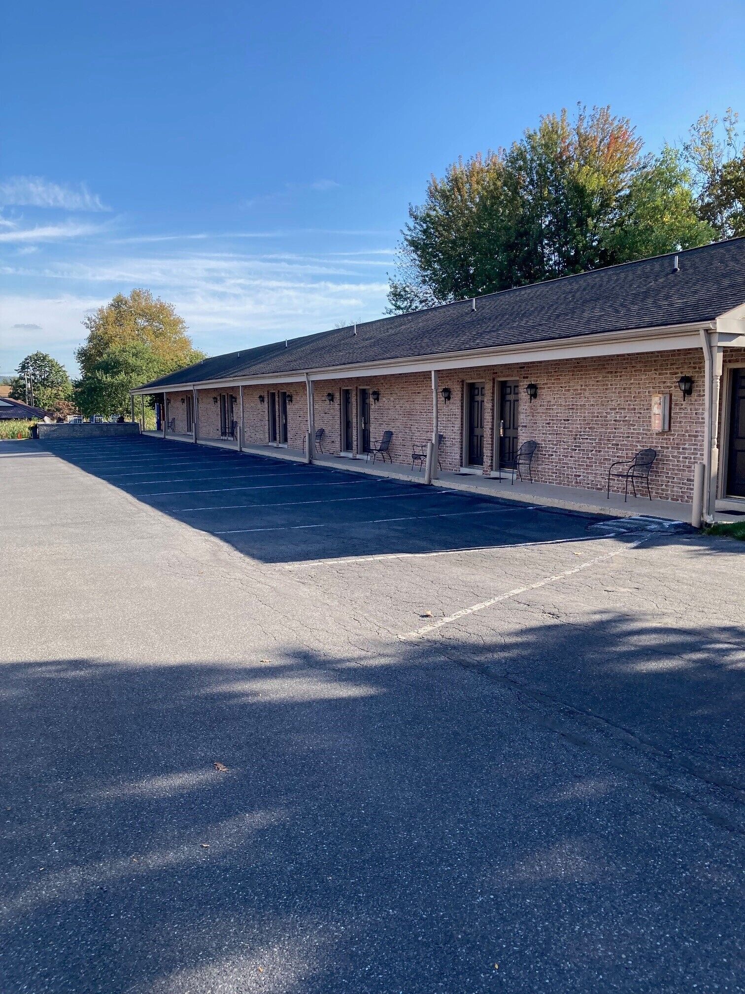 A row of motel rooms with a covered outdoor area and a parking lot.