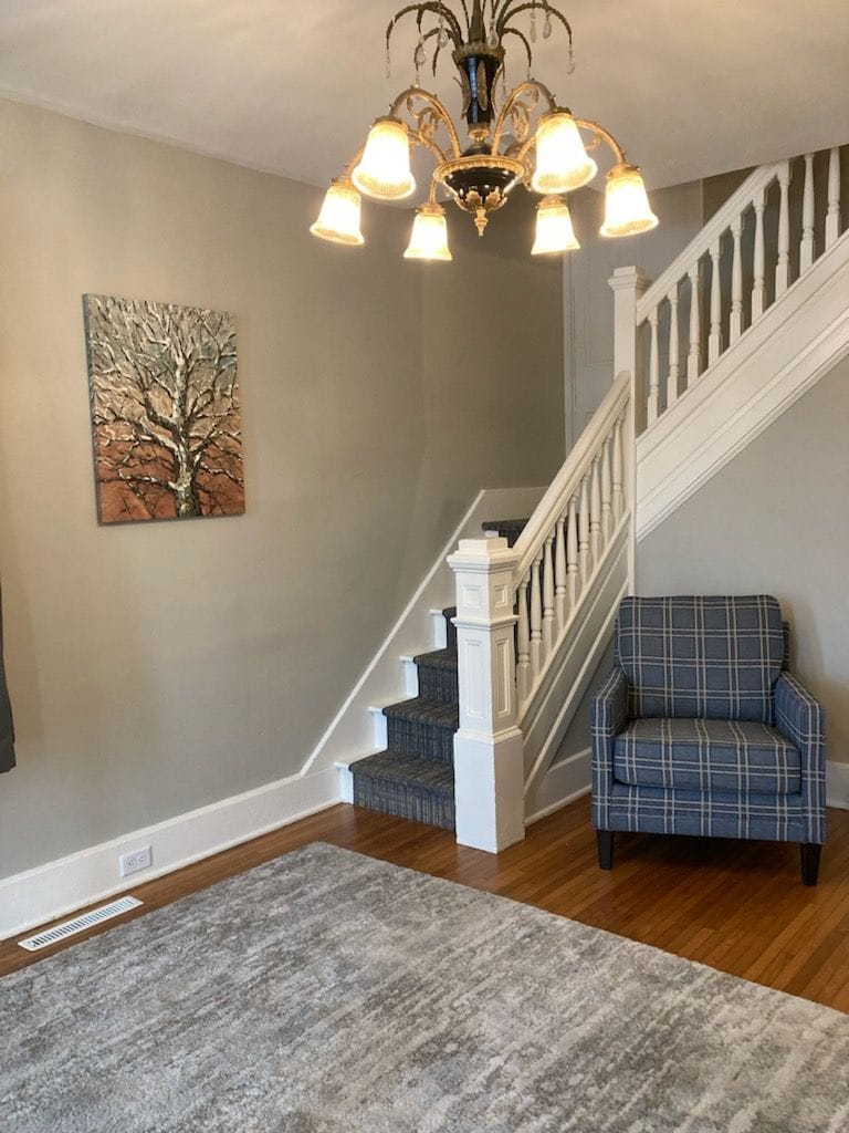 A staircase with white balusters, a blue plaid armchair, and a chandelier with multiple lights.
