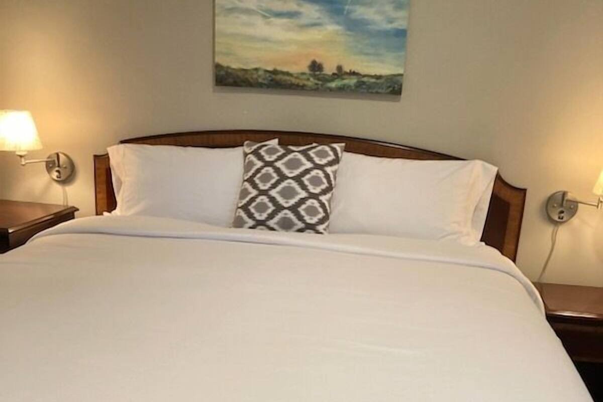 A neatly made bed with white linens and a patterned pillow, flanked by two bedside lamps.
