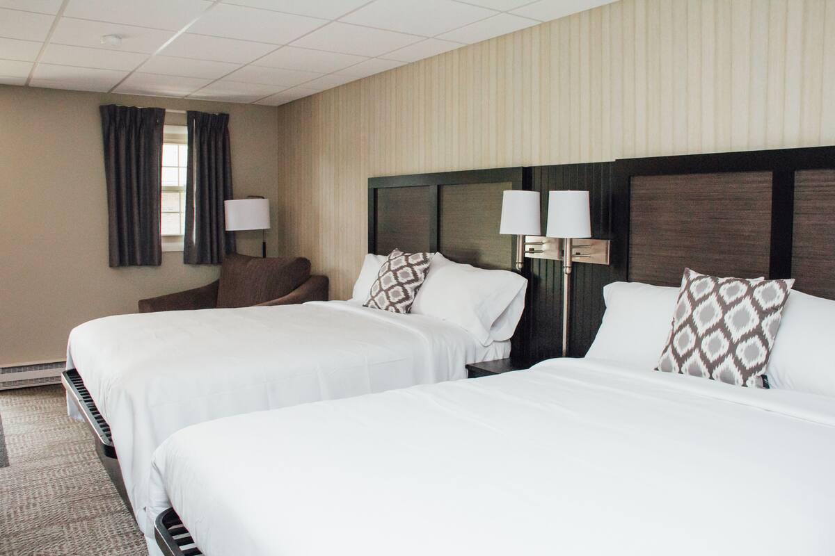 A hotel room with two beds, a chair, and two bedside lamps.