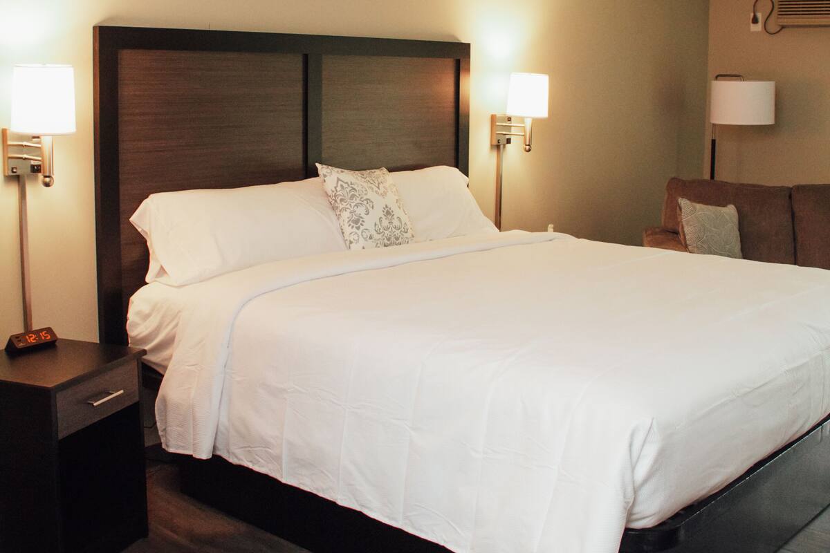 A neatly made bed with white linens, two bedside lamps, a wooden headboard, and a nightstand with a clock.