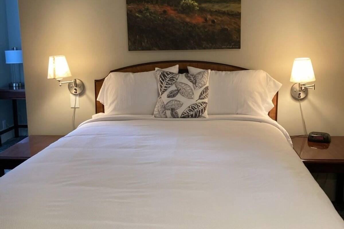 A neatly made bed with white linens and a decorative pillow, flanked by two bedside lamps.