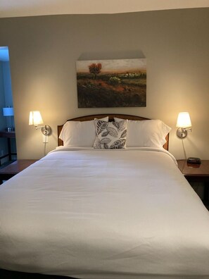 A neatly made bed with white linens and a decorative pillow, flanked by two bedside lamps. - Country Squire Inn and Suites (New Holland)
