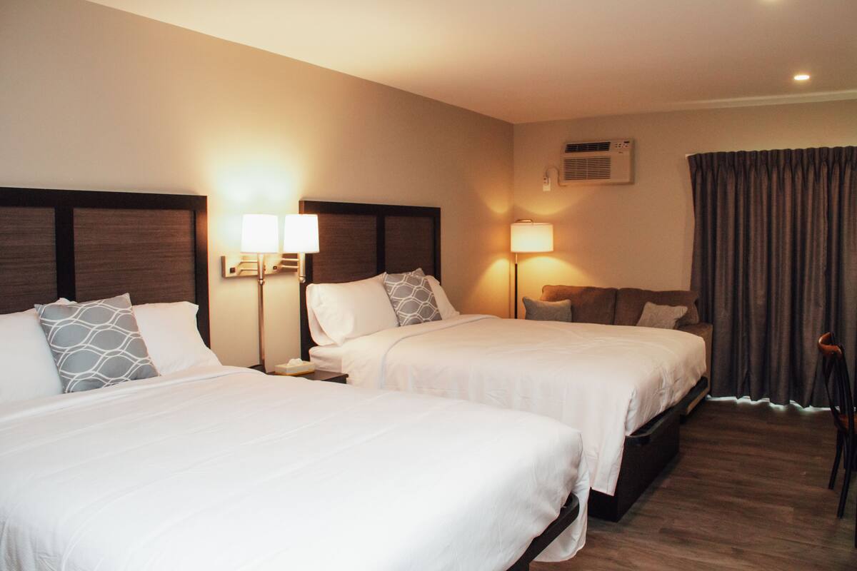 A hotel room with two beds, nightstands, lamps, an air conditioning unit, and a curtain.