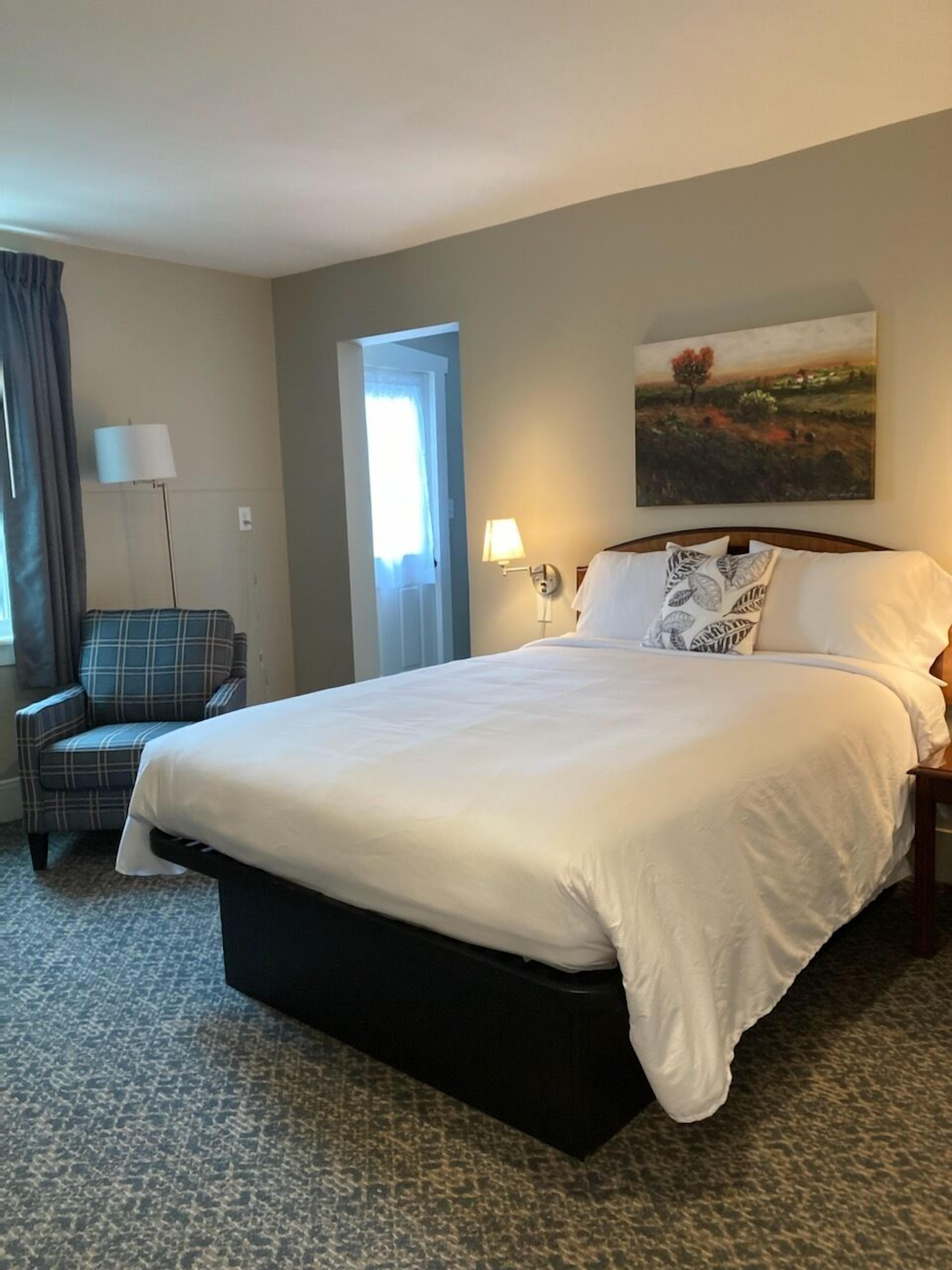 A hotel room with a large bed, a chair, a painting on the wall, and a lamp.
