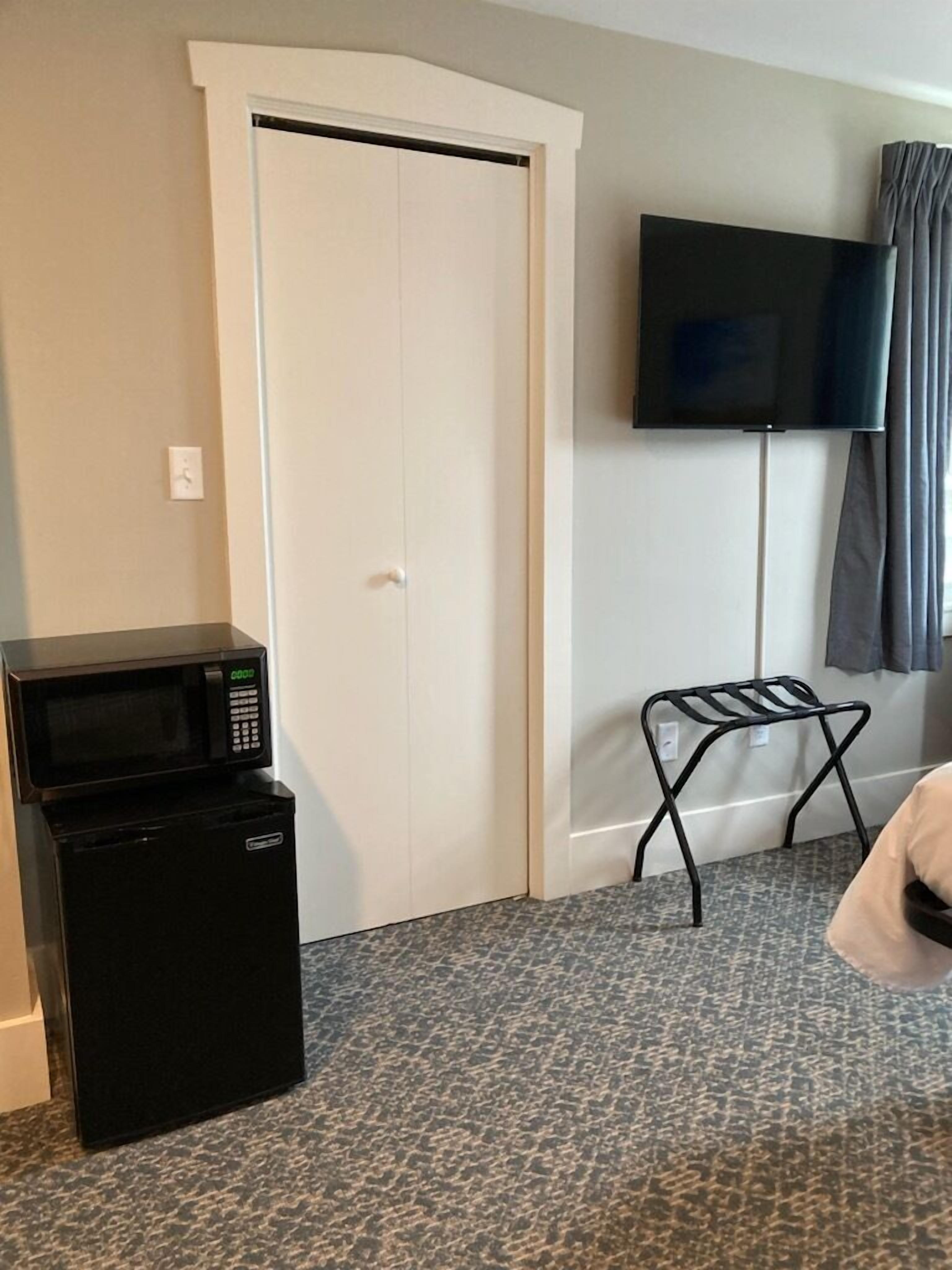 A hotel room with a closed white door, a flat-screen TV mounted on the wall, a black microwave, and a small black table.