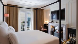A hotel room with a four-poster bed, a television, a fireplace, and a balcony with a view.