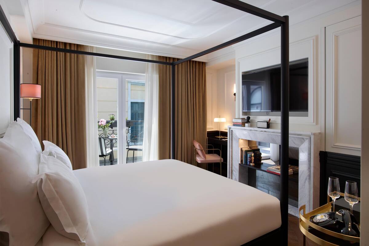A hotel room with a four-poster bed, a television, a fireplace, and a balcony with a view.