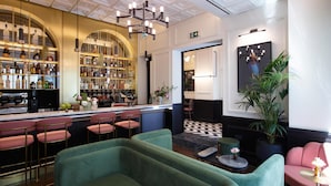 A bar area with a curved shelf displaying bottles, a chandelier, and seating with a checkered floor.