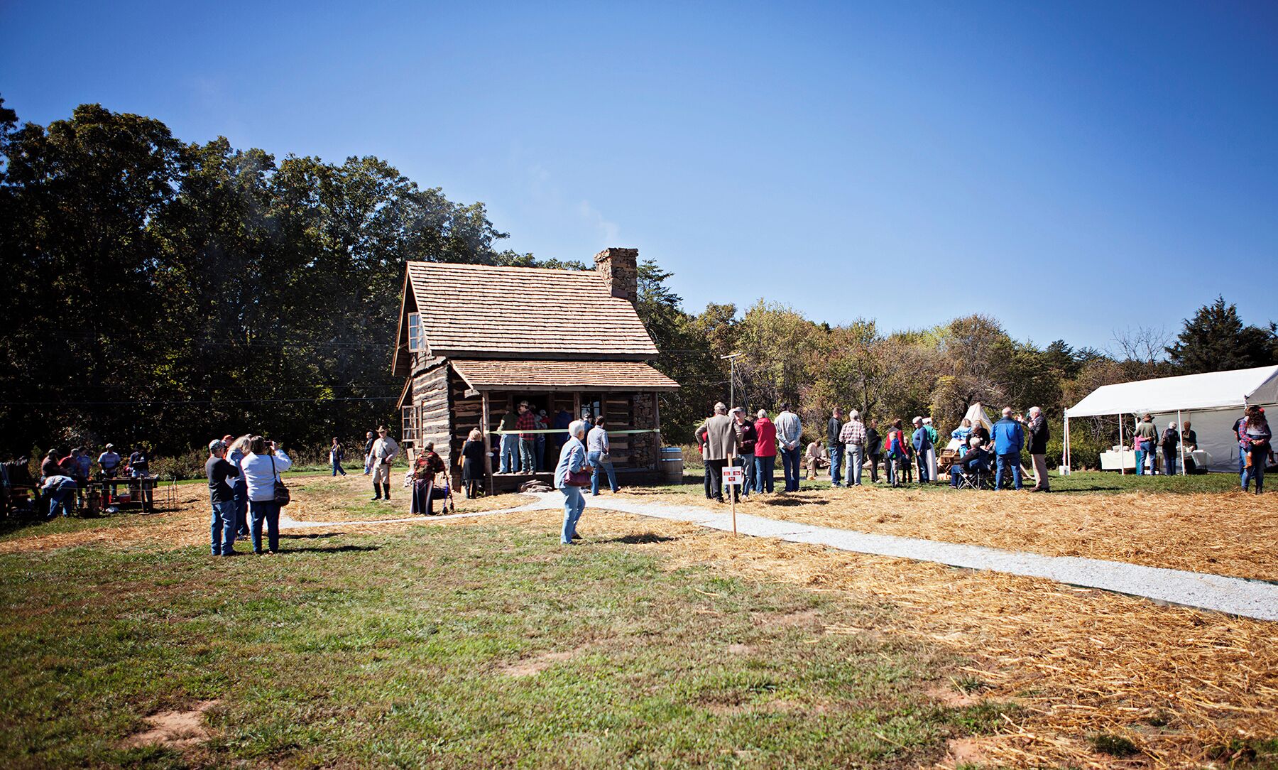 A rustic log cabin with a dirt path leading to it, surrounded by a grassy area with trees.
