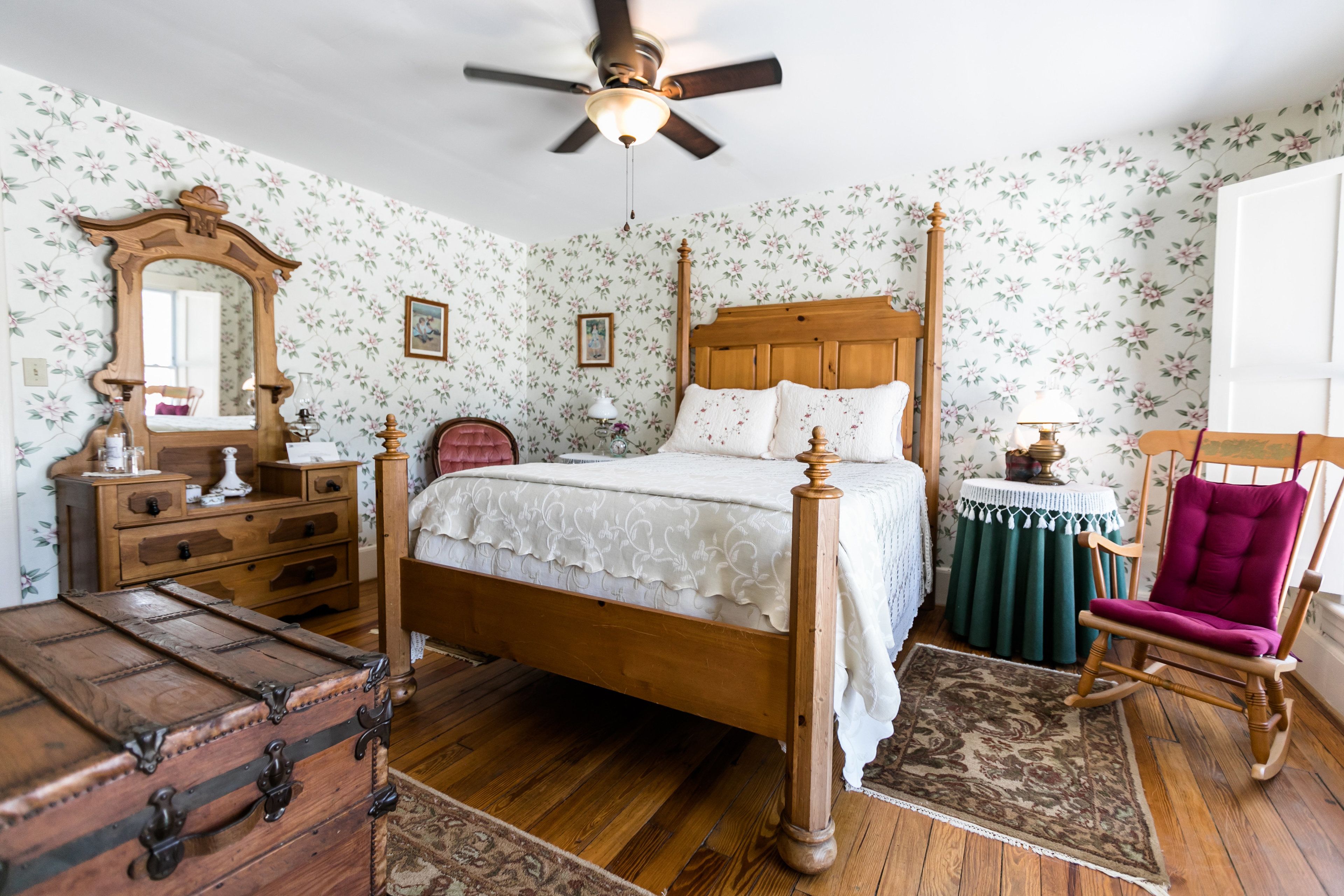 A bedroom with a wooden four-poster bed, a dresser, a chair, and a trunk.