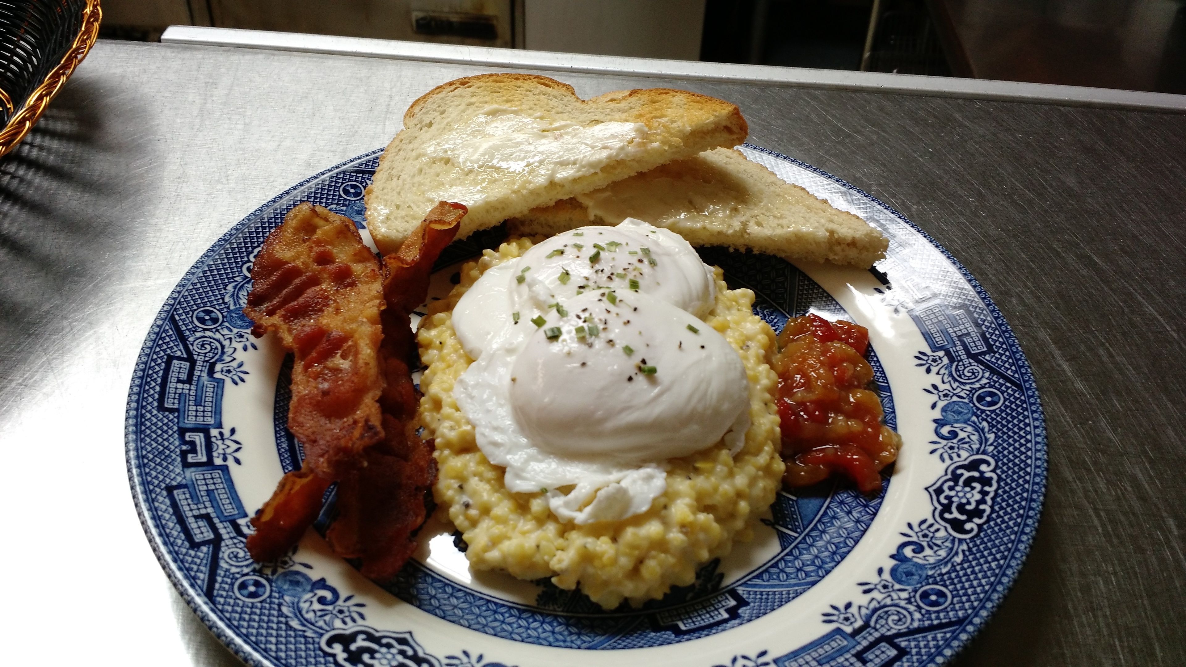 A plate with scrambled eggs, bacon, toast, and tomato sauce.
