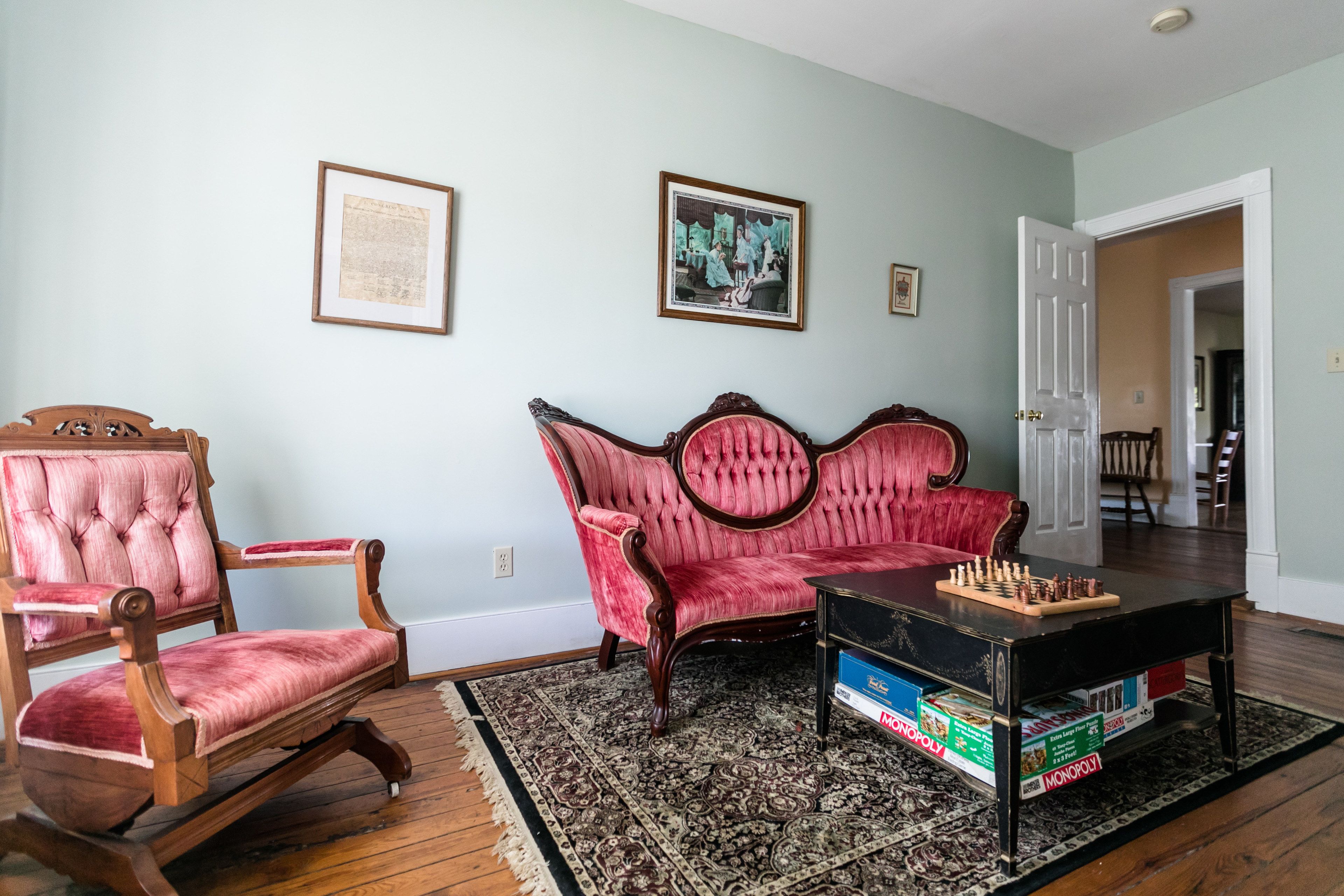 A living room with a red sofa, a wooden chair, and a coffee table with Monopoly games.