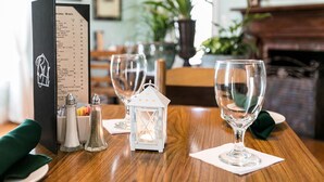 Une table de restaurant dressée avec un menu, des salières et des poivrières, une petite lanterne blanche et des verres à vin vides.