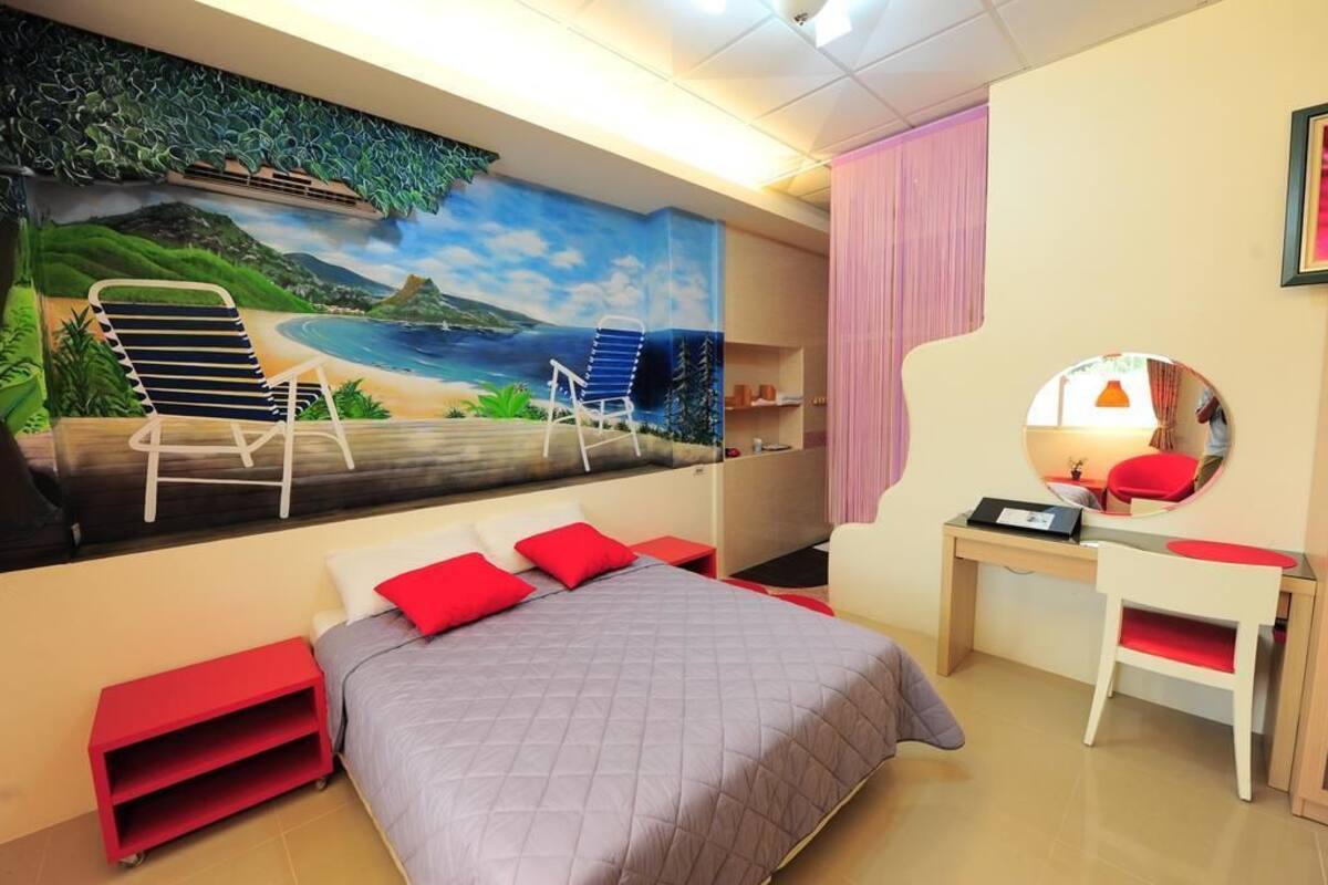 Un dormitori amb un llit, escriptori, cadira, mirall i un mural amb una escena de platja.