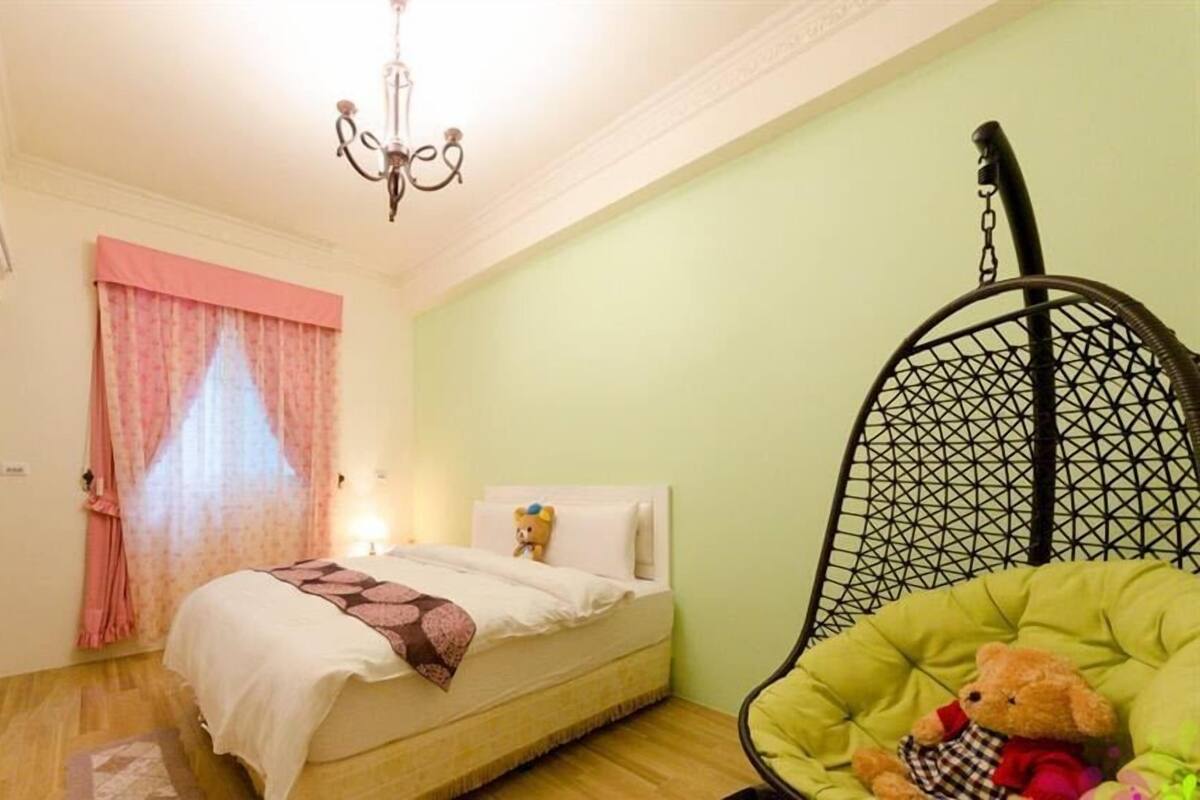 Un dormitorio con cama, una silla colgante, un osito de peluche y una araña.